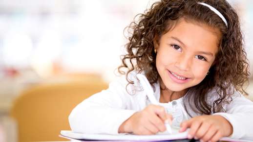 Image of a little girl smiling and writing.