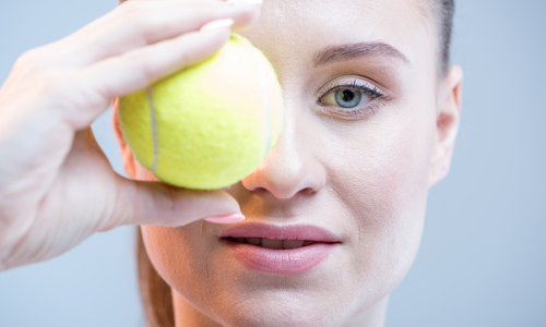 Woman with tennis ball covering eye