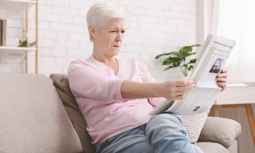 Woman squinting while reading the newspaper